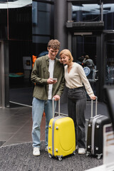 happy young couple with travel bags looking at mobile phone in hall of modern hotel.