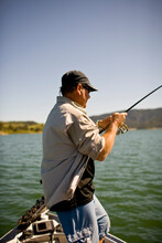 A Man Stands On A Boat With Fishing Pole In Hand While Bass Fishing In Lake Casitas.