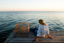 A Young Woman Rests Comfortably Sits On A Dock Overlooking The Calm Waters Of The Gulf Of Mexico.