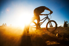 A Man On A Mountain Bike, Silhouetted By The Setting Sun.