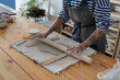 © DimaBerlin - Female potter artist rolling with pin raw clay. Woman ceramist in dirty apron prepare for shaping pottery. Craftswoman hands work with earthenware. Art studio production and craftsmanship therapy