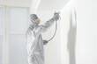 © New Africa - Decorator in protective overalls painting wall with spray gun indoors