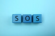 © New Africa - Abbreviation SOS (Save Our Souls) made of cubes with letters on light blue background, top view