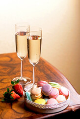 two glasses of champagne and macarons with strawberries on a wooden table