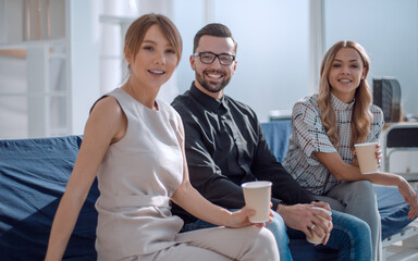 Poster - young employee with her colleagues sitting in the office lobby