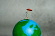 Miniature people toy figure photography. Women news presenter standing above earth globe presenting weather forecast. Grey cloudy background