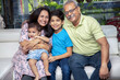 © GAJENDRRA BHATI  - Portrait of Happy indian grand parents sitting with their grand children at home. Asian senior and young couple with kids looking at camera.