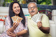 © GAJENDRRA BHATI  - Happy mature senior Indian couple holding money rupee notes in hand while sitting at home. Savings and banking concept