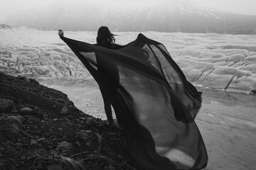 Wall Mural - Graceful lady with waving fabric sheet monochrome scenic photography. Picture of person with high glacier on background. High quality wallpaper. Photo concept for ads, travel blog, magazine, article