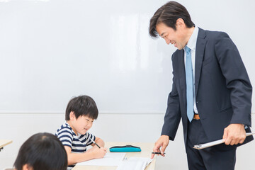 小学生に授業で勉強を教える笑顔の塾講師・先生（夏期講習・日本人男性）
