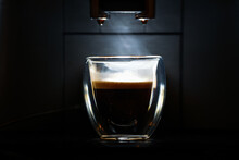 Steams coming out from an espresso coffee in a double-walled glass cup against dark background. Fresh coffee made from an espresso machine.