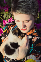 Poster - Close up woman with haircut holding puppy in garden portrait picture. Closeup front view photography with blossom on background. High quality photo for ads, travel blog, magazine, article