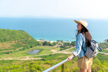 Wall Mural - Asian woman with backpack solo travel on tropical island mountain peak in summer sunny day. Attractive girl enjoy and fun outdoor lifestyle looking beautiful nature of ocean on beach holiday vacation.