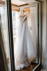 Wall Mural - Fashionable beautiful lace wedding dress hanging on hanger in hotel room. morning preparation wedding concept. vintage wedding gown.