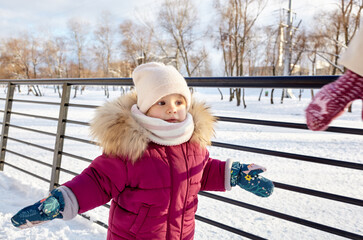 Mother and daughter are walking in the winter city park on Christmas and New Year holidays. Parent and little child having fun outdoors