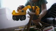 © Marco - Kid plays with bulldozer tractor toy picking pieces of wood playing at home playroom. Closeup child hands