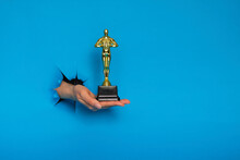 Hollywood Golden Oscar Academy Award Statue In Hand Isolated On White Background. Success And Victory Concept.