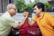© GAJENDRRA BHATI  - Portrait of indian senior father and young son Arm wrestling with each other at home.
