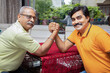 © GAJENDRRA BHATI  - Portrait of happy indian senior father and young son Arm wrestling with each other at home. Looking at camera
