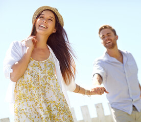 Wall Mural - Happy, young couple and holding hands with smile for summer vacation, travel or journey together in the outdoors. Beautiful woman leading her boyfriend by the hand on a sunny day for the holiday