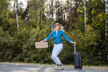 Laughing Active Cheerful Blond Female Hitchhiker In Dance Squat Position Hold Carton Board Anywhere With Luggage By Road