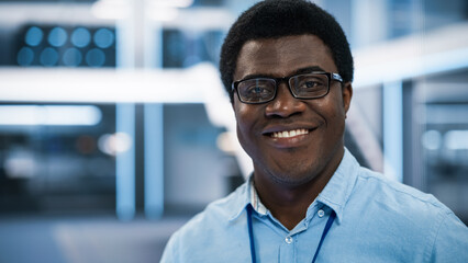 Poster - Handsome African Man Wearing Glasses and a Blue Shirt Smiling and Looking at Camera. Young Black Man Working as Engineer or Scientist in Technology Research Facility. Close Up Portrait.