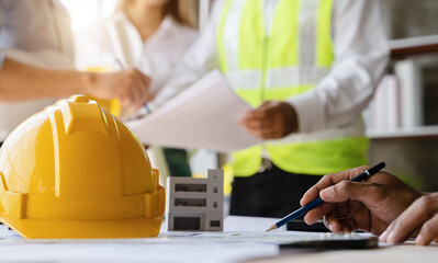 Yellow hard hat on workbench with Engineer teams meeting working together wear worker helmets hardhat on construction site. Asian industry professional team