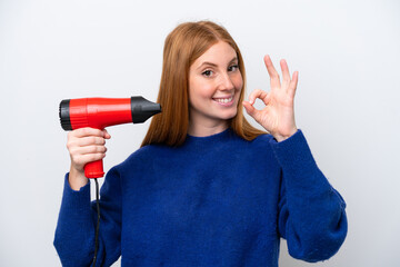 Wall Mural - Young redhead woman holding a hairdryer isolated on white background showing ok sign with fingers