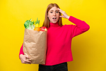 Wall Mural - Young redhead woman holding a grocery shopping bag isolated on yellow background with surprise expression