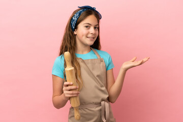 Wall Mural - Little caucasian girl holding a rolling pin isolated on pink background extending hands to the side for inviting to come