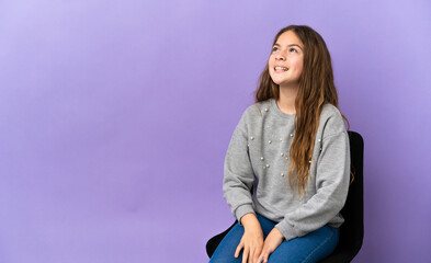 Wall Mural - Little caucasian girl sitting on a chair isolated on purple background laughing