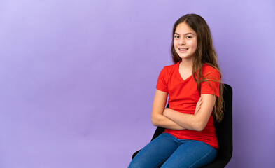 Wall Mural - Little caucasian girl sitting on a chair isolated on purple background with arms crossed and looking forward