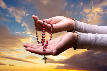 Wall Mural - Woman's hands in prayer sign with rosary on sky background