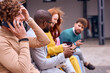 © Roman - happy businesspeople walking, sitting on bench, using smartphones. young Caucasian and african colleagues chatting. focus on curly european guy talking on phone. outside of office. business people