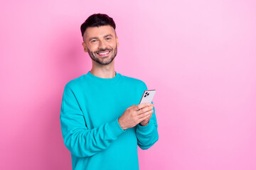 Poster - Photo of positive man toothy smile hold use telephone empty space isolated on pink color background