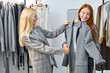 © Roman - Young affable caucasian fashion consultant joyfully helping to choose trendy jacket to beautiful redhead female customer in modern store, outfits on hangers in background. two ladies have nice talk