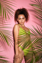 Lovely Female On Exotic Resort Having Good Mood Relaxing Resting In Swim Wear Isolated Pink Color Studio Background. Curly Caucasian Female With Fit Body In Green Swimwear With Tropical Exotic Plants