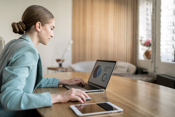 A business woman checking documents in a shirt, using a laptop in the office, monitoring the report online