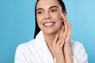 Wall Mural - Portrait of attractive young woman in bathrobe on light blue background. Spa treatment