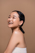 © LIGHTFIELD STUDIOS - Pleased asian woman in top looking away isolated on brown.