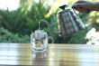 Woman pouring hot water into glass cup with drip coffee bag from kettle at wooden table, closeup