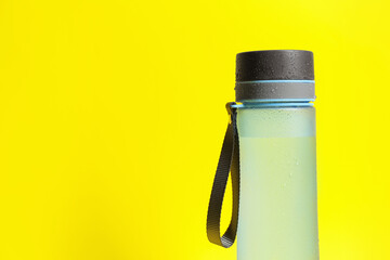 Sticker - Stylish closed bottle with water drops on yellow background, closeup. Space for text