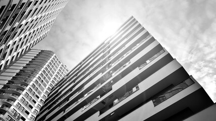 The narrow passage between modern residential buildings. Walls of high-rise apartment buildings and a narrow strip of sky between them. Modern urban living districts. Bottom view. Black and white.