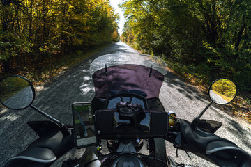 View from the first person, driving a tourist motorcycle on the road in the autumn forest. Freedom and travel transportation concept