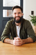 © Wavebreak Media - Portrait of biracial bearded young man wearing jacket with hands clasped sitting at table