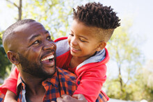 Happy African American Father And Son Embracing And Smiling In Their Backyard