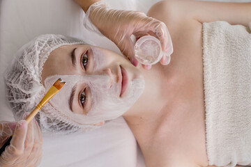 Wall Mural - A beautician applies a mask to the skin of a woman's face for therapeutic purposes. Rejuvenation, acne treatment