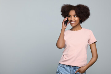 Wall Mural - Smiling African American woman talking on smartphone against light grey background. Space for text