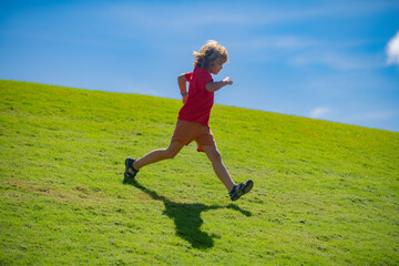 Sporty kid boy running on green grass and blue sky. Morning running with children. Child runner running in the nature. Morning jogging. Active healthy kids lifestyle.