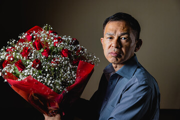 Middle-aged Asian man sending red roses and hazel to his loving wife. Concept photo of wedding anniversaries, entrance ceremonies and daily appreciation.